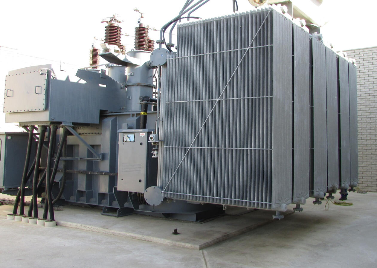 Power Transformers Grey power transformer with cooling fins and electrical bushings.